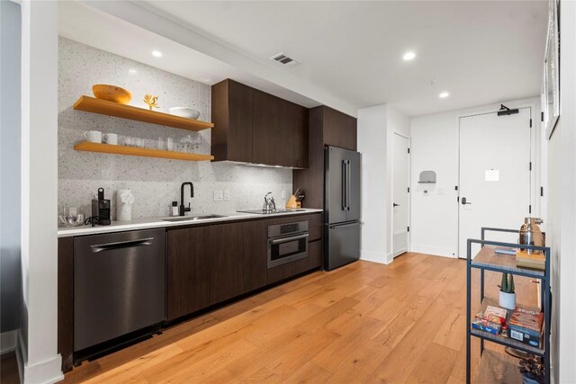 kitchen featuring sink, stainless steel appliances, backsplash, dark brown cabinets, and light wood-type flooring