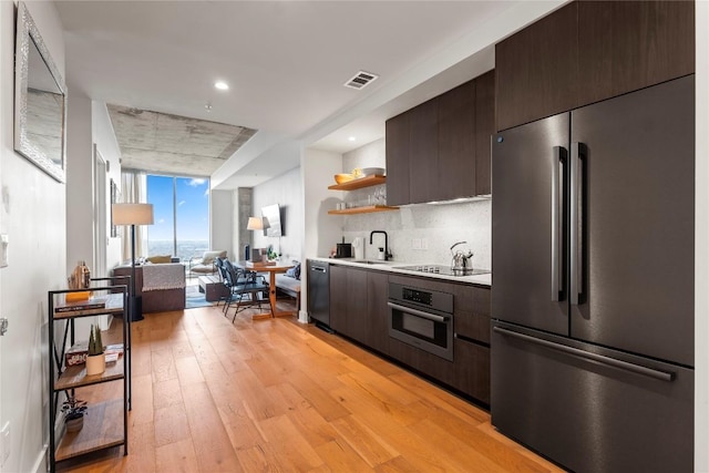 kitchen featuring light wood-type flooring, backsplash, dark brown cabinetry, stainless steel appliances, and sink