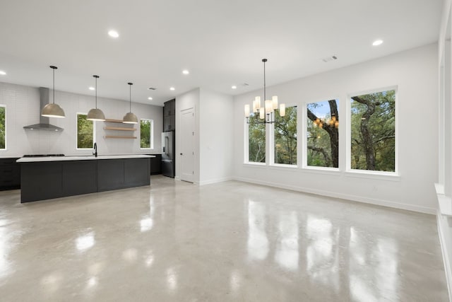 kitchen featuring backsplash, wall chimney range hood, stainless steel fridge, a large island, and a chandelier