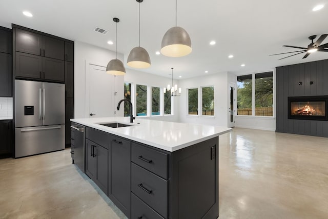 kitchen with sink, hanging light fixtures, a kitchen island with sink, a fireplace, and appliances with stainless steel finishes