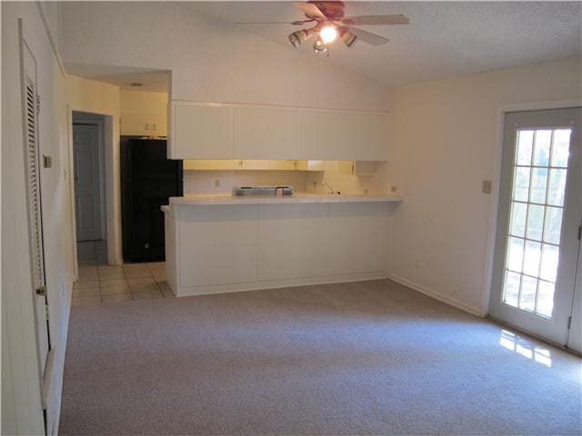 kitchen with lofted ceiling, light carpet, black fridge, kitchen peninsula, and white cabinetry