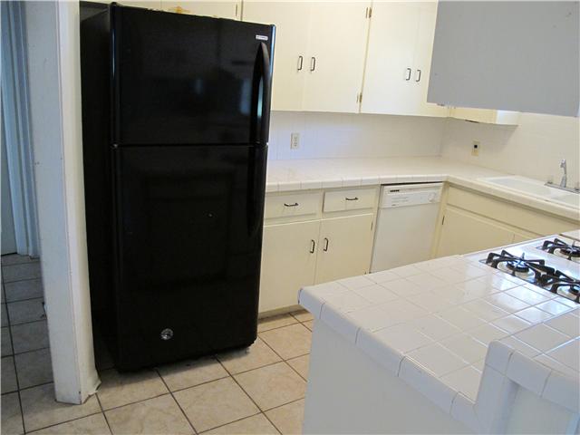 kitchen featuring black fridge, white dishwasher, sink, light tile patterned floors, and tile counters