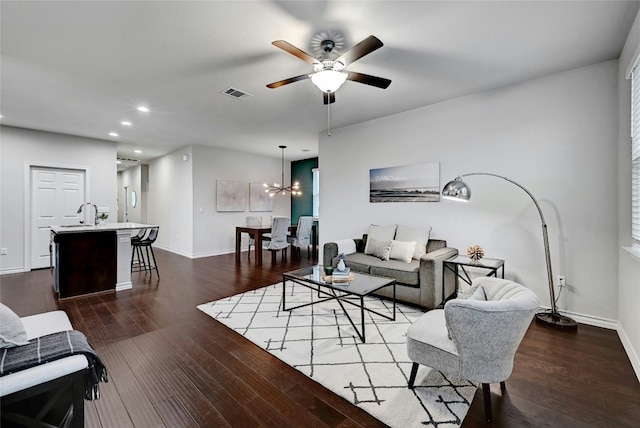 living room with ceiling fan with notable chandelier and dark hardwood / wood-style flooring