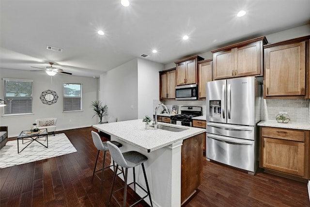 kitchen with decorative backsplash, appliances with stainless steel finishes, dark wood-type flooring, sink, and a center island with sink