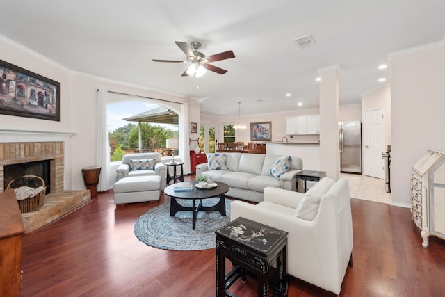 living room with a brick fireplace, ceiling fan, crown molding, sink, and hardwood / wood-style floors