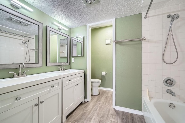 full bathroom with vanity, a textured ceiling, tiled shower / bath combo, wood-type flooring, and toilet