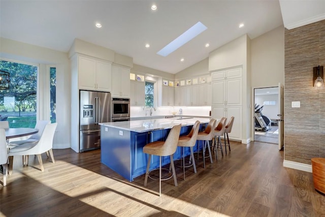 kitchen with light stone countertops, appliances with stainless steel finishes, dark hardwood / wood-style floors, white cabinetry, and a large island