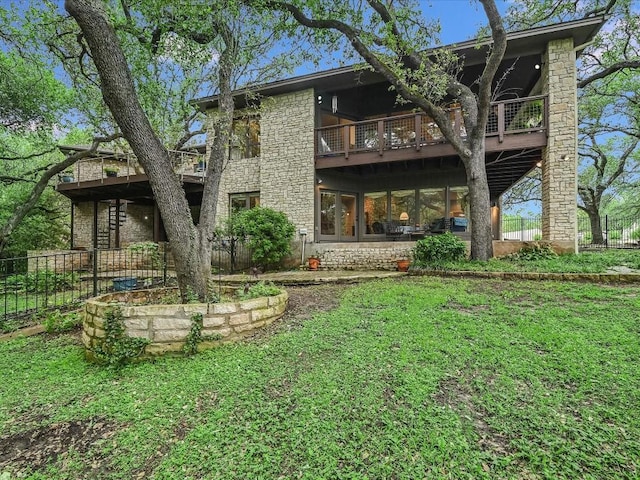 rear view of house featuring stone siding, a lawn, a balcony, and fence