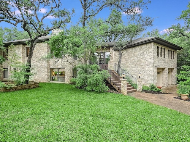 back of house with stairs, a garage, a yard, stone siding, and driveway