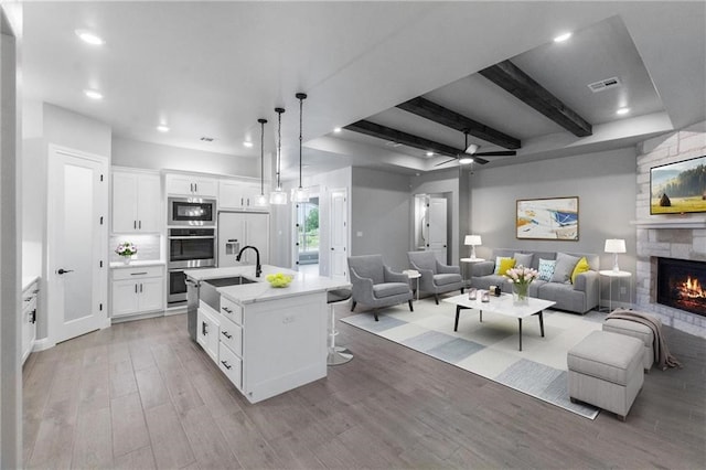 kitchen featuring pendant lighting, stainless steel appliances, an island with sink, and white cabinets