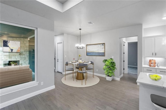 dining space featuring a stone fireplace, a chandelier, and light hardwood / wood-style floors