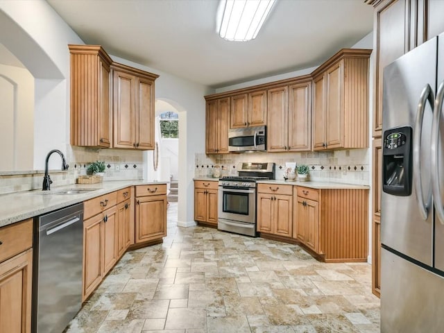 kitchen featuring backsplash, light stone counters, sink, and appliances with stainless steel finishes