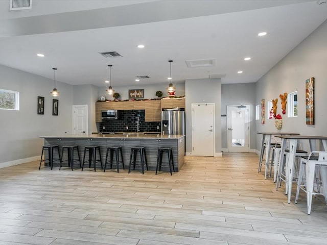 kitchen featuring a breakfast bar, appliances with stainless steel finishes, decorative light fixtures, and tasteful backsplash