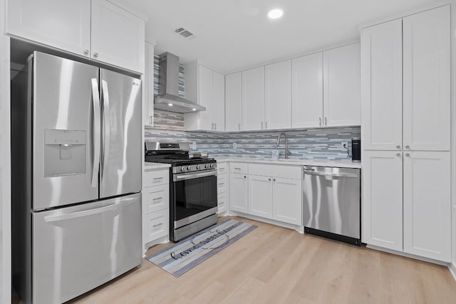 kitchen featuring sink, stainless steel appliances, wall chimney range hood, light hardwood / wood-style flooring, and white cabinets