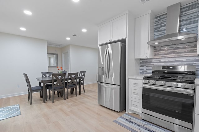 kitchen featuring decorative backsplash, wall chimney exhaust hood, stainless steel appliances, white cabinets, and light hardwood / wood-style floors