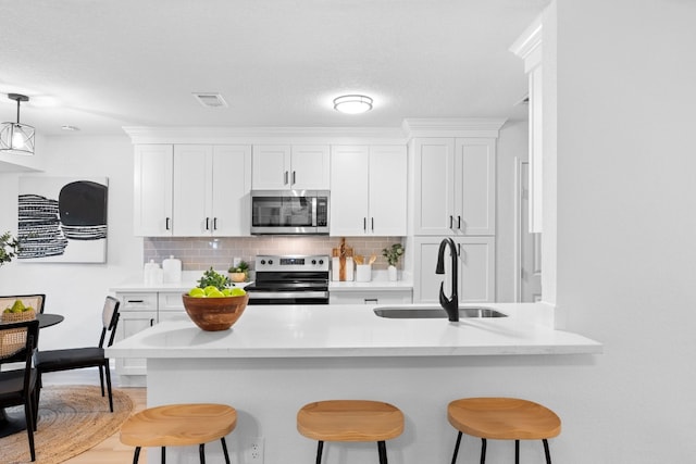 kitchen with appliances with stainless steel finishes, sink, a breakfast bar area, white cabinets, and backsplash