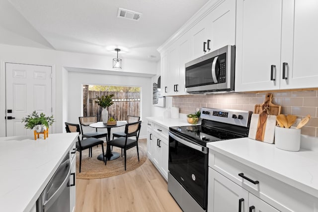 kitchen with white cabinetry, light stone counters, light hardwood / wood-style flooring, appliances with stainless steel finishes, and backsplash