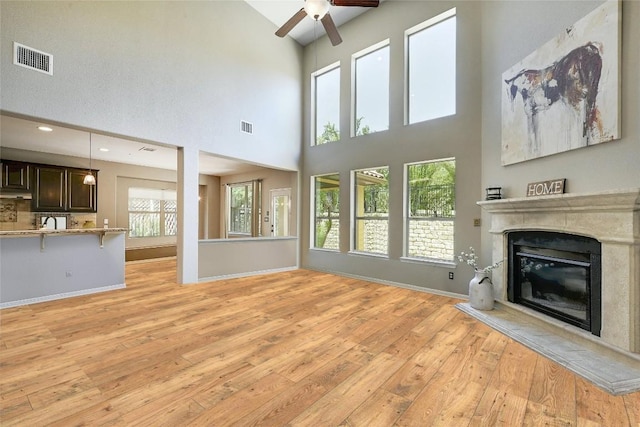 unfurnished living room featuring ceiling fan, a high ceiling, and light wood-type flooring