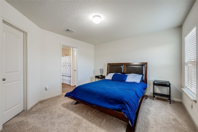 carpeted bedroom with ensuite bathroom and a textured ceiling