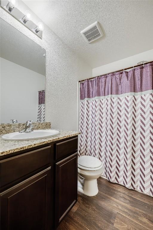 bathroom featuring vanity, toilet, a textured ceiling, curtained shower, and wood-type flooring