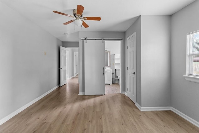 unfurnished bedroom featuring a barn door, ceiling fan, and light hardwood / wood-style floors