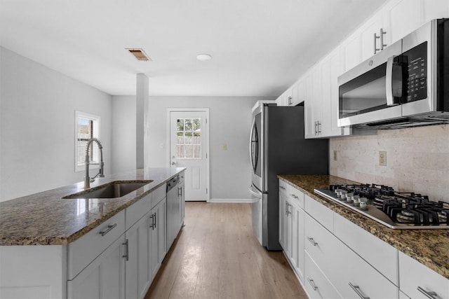 kitchen featuring dark stone counters, white cabinets, sink, light hardwood / wood-style flooring, and stainless steel appliances