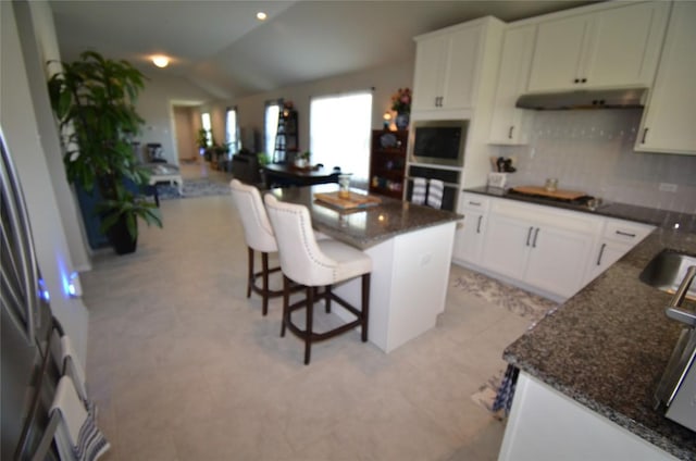 kitchen featuring a kitchen bar, a kitchen island, dark stone countertops, oven, and lofted ceiling