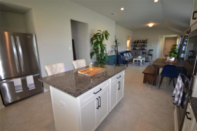 kitchen featuring a center island, white cabinetry, stainless steel refrigerator, and dark stone counters