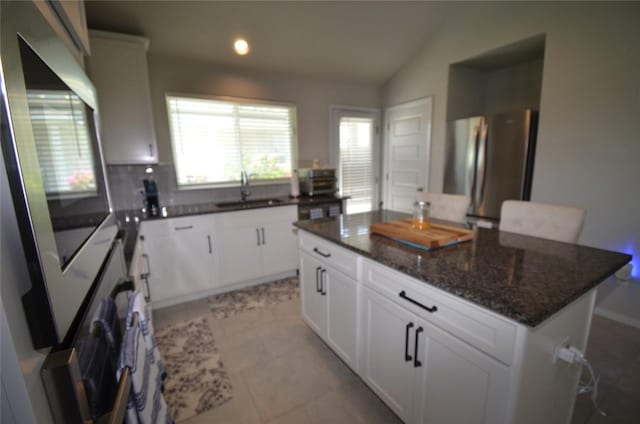 kitchen featuring white cabinets, stainless steel fridge, sink, and vaulted ceiling