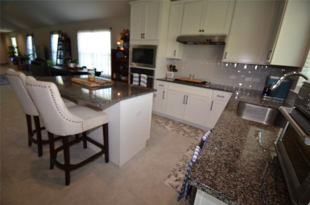 kitchen with a kitchen breakfast bar, sink, dark stone countertops, black oven, and a kitchen island