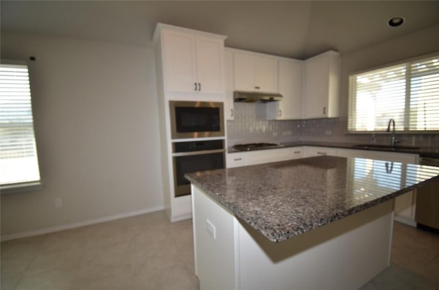 kitchen with under cabinet range hood, a sink, tasteful backsplash, white cabinetry, and stainless steel appliances