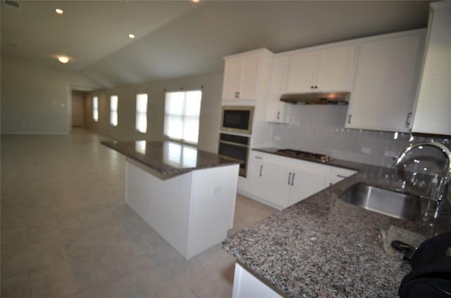 kitchen with a center island, under cabinet range hood, dark stone countertops, stainless steel appliances, and a sink