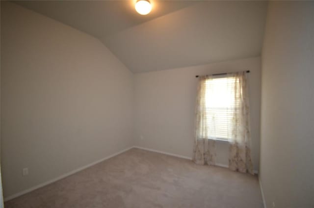 spare room featuring baseboards, lofted ceiling, and light colored carpet