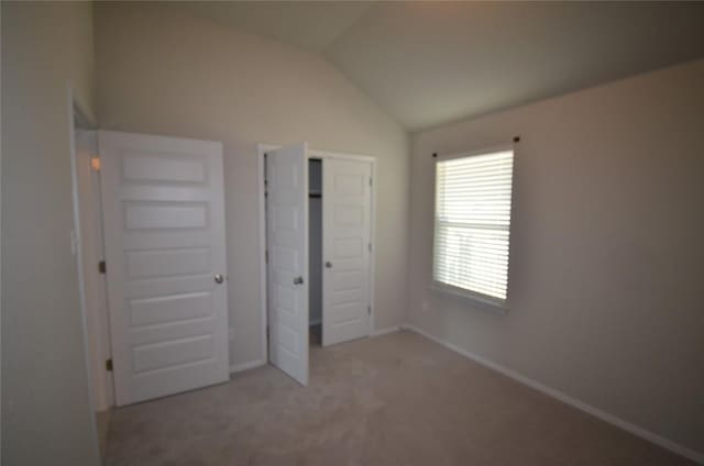 unfurnished bedroom featuring a closet, light colored carpet, baseboards, and vaulted ceiling