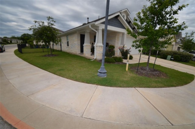 view of property exterior with stone siding, a lawn, concrete driveway, and fence