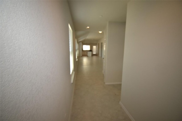 hallway featuring a textured wall and baseboards