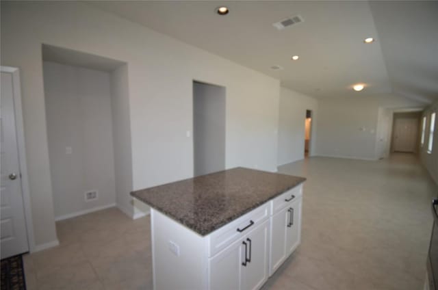 kitchen with dark stone countertops, a kitchen island, recessed lighting, white cabinets, and vaulted ceiling