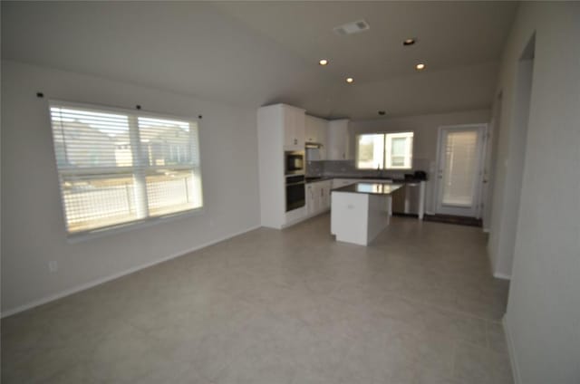 kitchen with a center island, baseboards, open floor plan, vaulted ceiling, and white cabinets