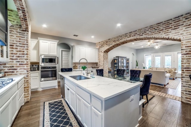 kitchen featuring sink, a kitchen island with sink, stainless steel appliances, light stone countertops, and white cabinets