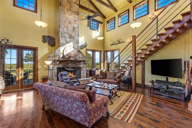 living room with beam ceiling, a stone fireplace, a healthy amount of sunlight, and a towering ceiling