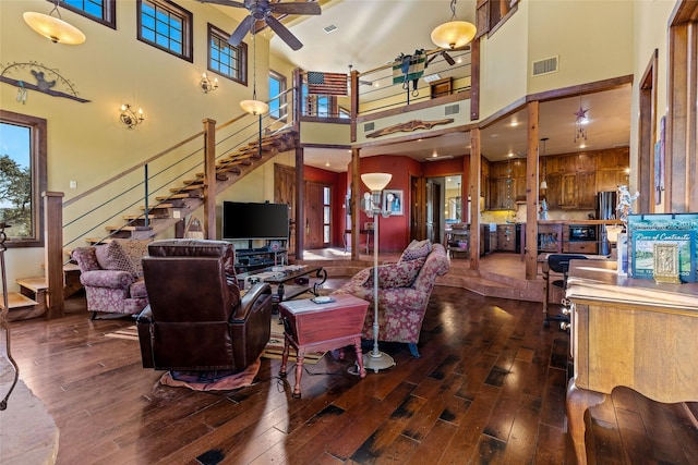 living room with dark wood-type flooring, a towering ceiling, and ceiling fan