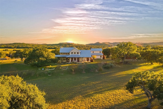 back house at dusk featuring a mountain view, a lawn, and a rural view