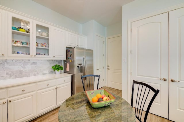 kitchen with light stone countertops, light wood-type flooring, tasteful backsplash, stainless steel fridge with ice dispenser, and white cabinetry