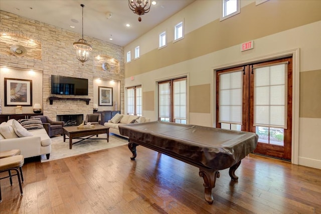 rec room featuring a notable chandelier, a stone fireplace, light wood-type flooring, and pool table