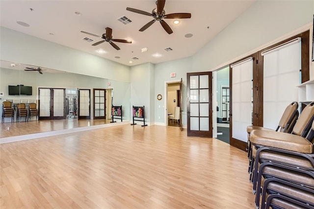 exercise room featuring ceiling fan, french doors, a towering ceiling, and light hardwood / wood-style flooring