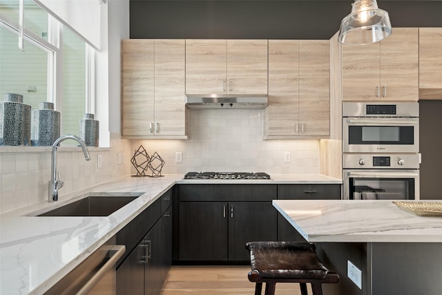 kitchen featuring light stone counters, sink, decorative light fixtures, and appliances with stainless steel finishes