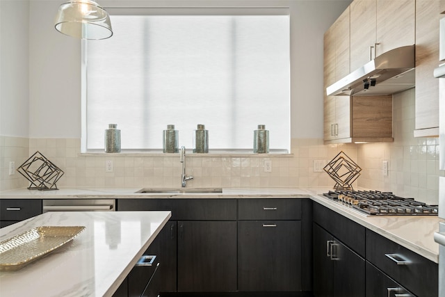 kitchen featuring sink, light stone counters, decorative backsplash, stainless steel gas cooktop, and decorative light fixtures