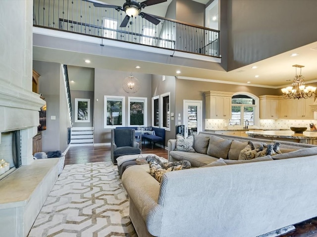 living room featuring ceiling fan with notable chandelier, crown molding, hardwood / wood-style flooring, a fireplace, and a high ceiling