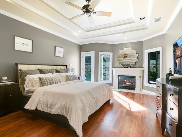 bedroom featuring dark hardwood / wood-style floors, ceiling fan, a raised ceiling, and ornamental molding