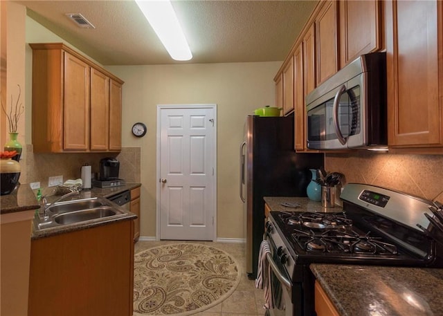 kitchen with sink, tasteful backsplash, dark stone countertops, light tile patterned floors, and appliances with stainless steel finishes